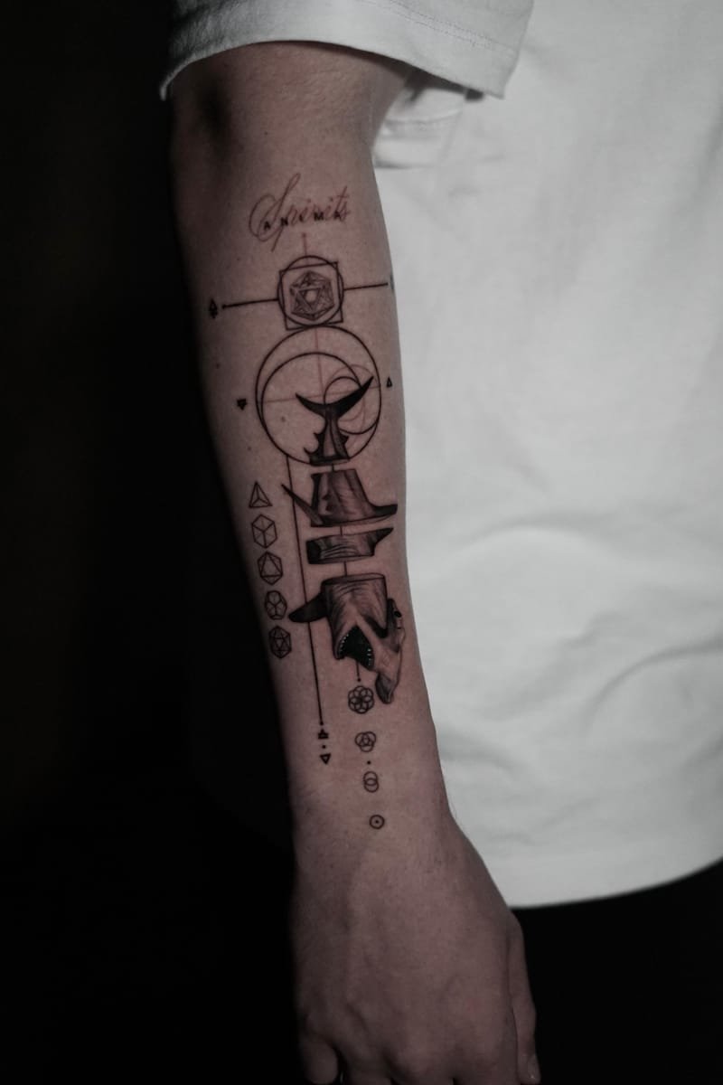 Plano medio del antebrazo tatuado: se distinguen los cinco sólidos geométricos alineados en el margen y el sombreado gris de la cola de ballena.