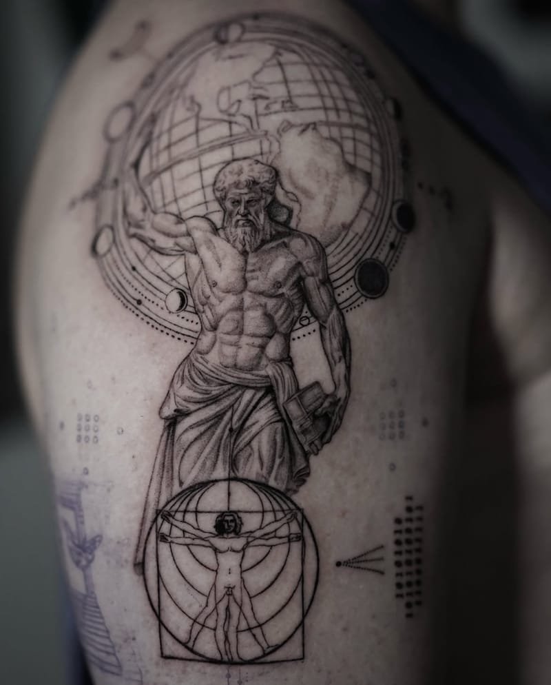Tatuaje en proceso en el hombro: Atlas, musculado y barbado, sostiene un globo terrestre con meridianos y continentes, rodeado de órbitas con fases de la luna; debajo, el Hombre de Vitruvio dentro de un círculo y un cuadrado, y a los lados columnas de puntos y de ceros y unos.