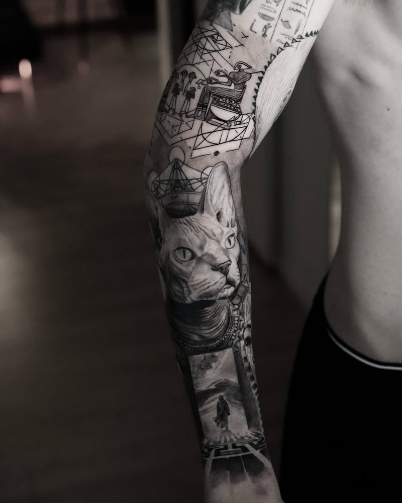 Brazo de perfil con una manga completa: jeroglíficos y una figura sentada en su trono, pirámides trazadas con geometría y el signo de la proporción áurea, un gato esfinge con collar de cuentas, una figura con túnica que camina por el desierto y una greca en la muñeca.