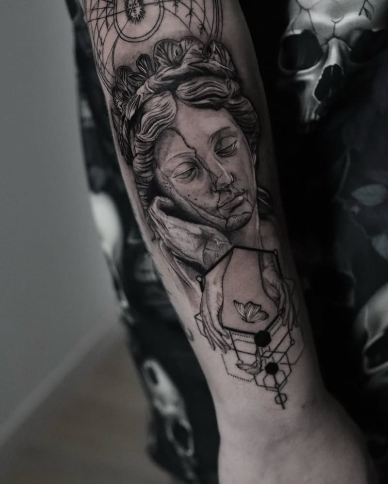 El antebrazo completo: el busto de mármol agrietado apoyado en una mano, la carta celeste con el sol encima y, debajo, dos manos que sostienen un hexágono con una mariposa, con geometría de hexágonos hasta la muñeca.