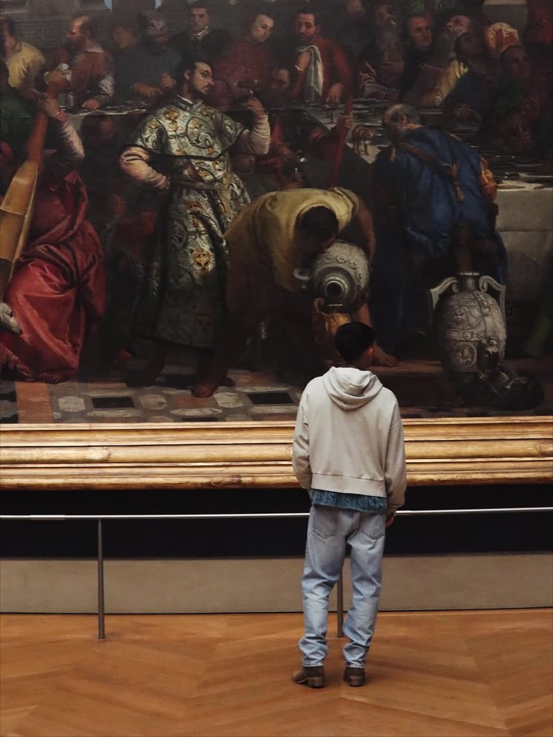 Tomás, de espaldas, ante Las bodas de Caná de Veronese, un lienzo monumental con marco dorado.