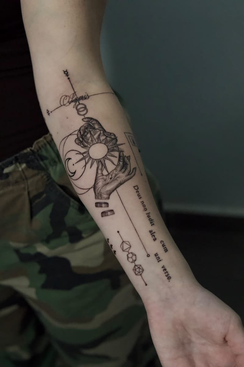 Plano más cercano del antebrazo: las manos sombreadas como un grabado, el sol y la luna, dos barras, los poliedros unidos por una línea y el texto latino en vertical.